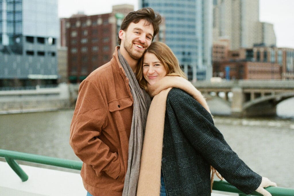 Downtown Grand Rapids film couples session on 35mm of couple hugging by riverwalk with city skyline in Michigan