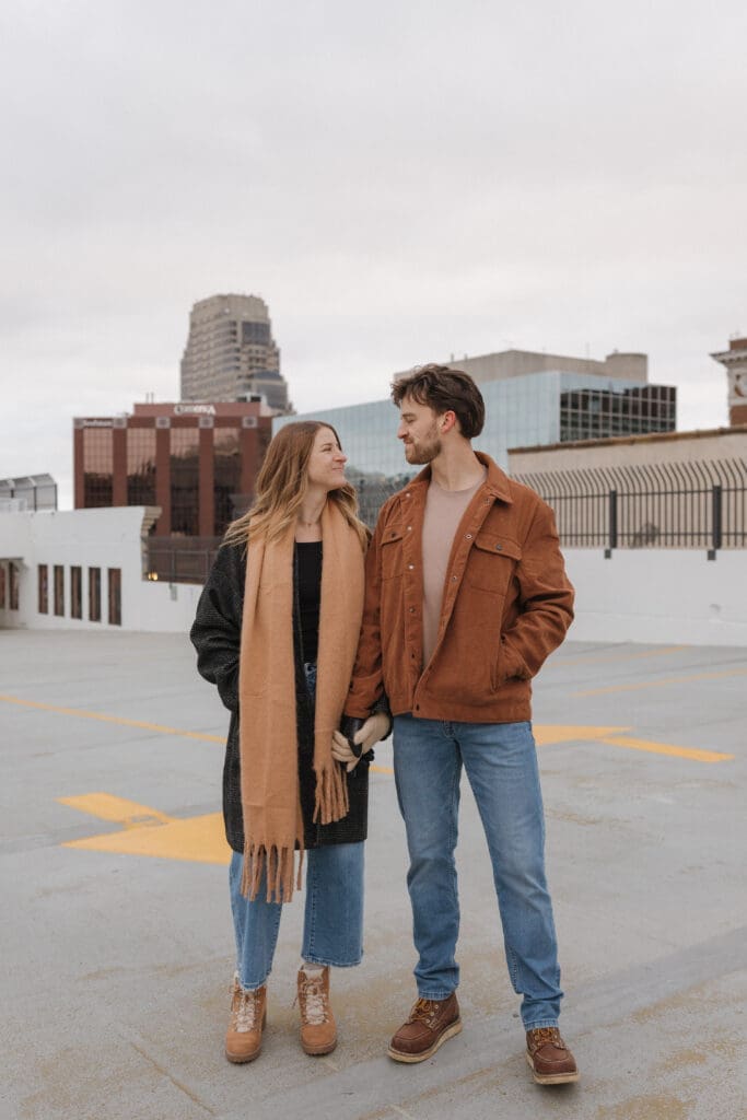 Downtown Grand Rapids winter couples session on rooftop parking garage with couple holding hands and city skyline in Michigan
