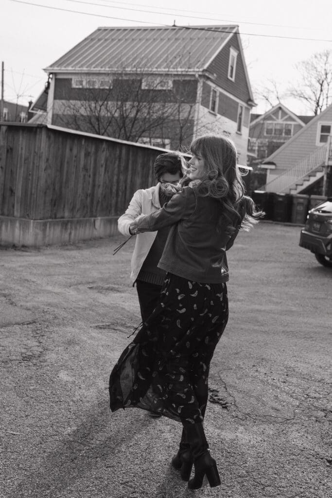 Eastown Grand Rapids engagement session in Michigan with candid black and white photo of couple spinning in urban neighborhood