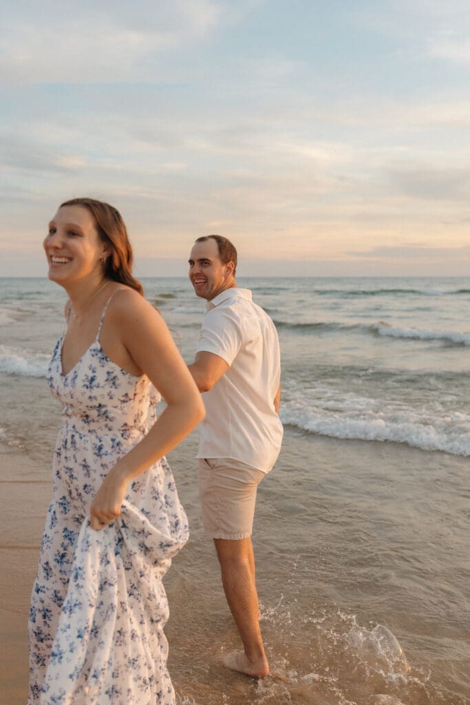 Lake Michigan beach engagement photos of couple walking in water at golden hour with waves and sunset light