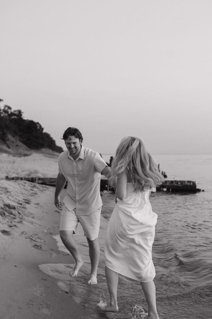 Lake Michigan engagement photos black and white of couple running along beach shoreline with waves