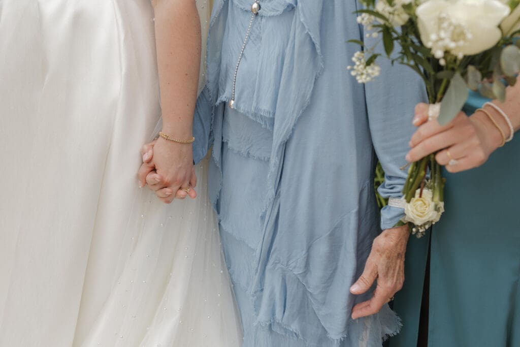 Bride, her sister, and grandmother holding hands during a summer wedding at New Vintage Place in Grand Rapids, Michigan