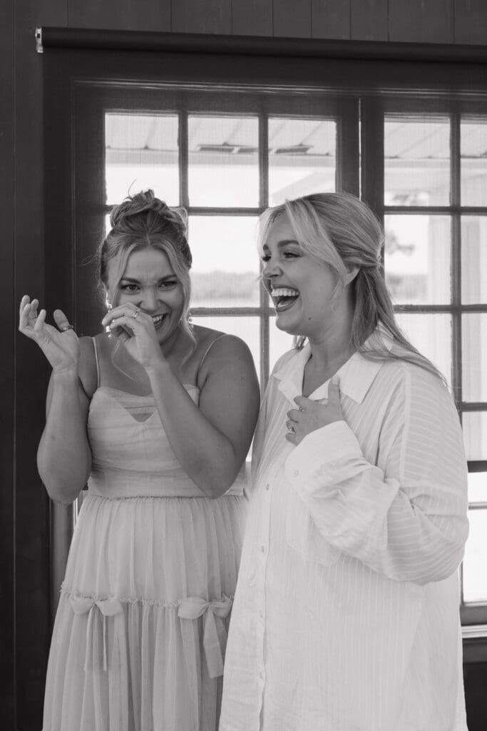 Black and white candid photo of a bride and bridesmaid laughing together while getting ready on the morning of a Walden Woods wedding in Michigan.