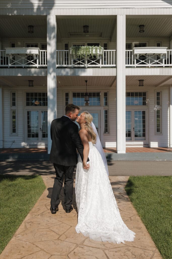 Bride and groom sharing a candid kiss while walking hand in hand after their wedding ceremony at Walden Woods in Michigan.