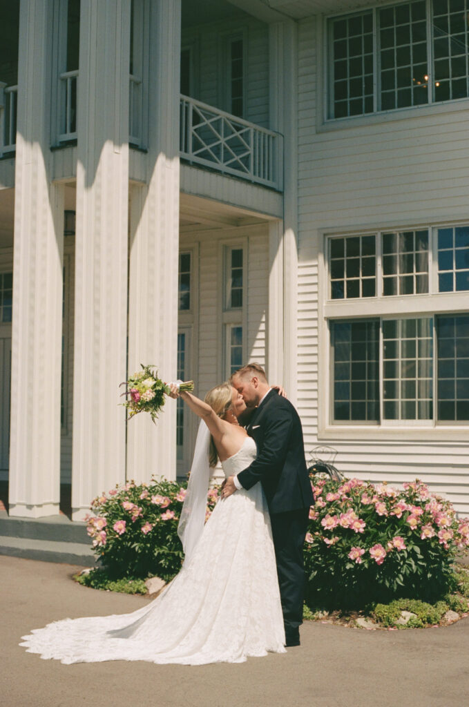 Bride and groom sharing a kiss outside Waldenwoods Resort in Hartland, Michigan during a sunny June wedding, captured on 35mm film with classic, candid wedding photography.