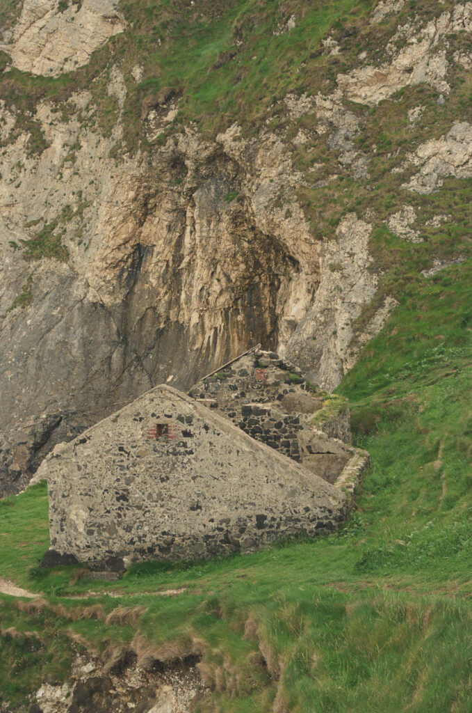 Historic stone building at the Kinbane Castle ruins beneath dramatic limestone cliffs on the Northern Ireland coastline, photographed on 35mm film.