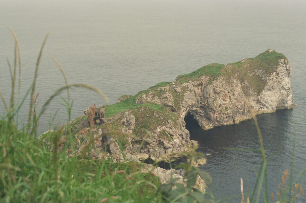 Elevated view of the Kinbane Castle ruins and rugged coastal cliffs along the Causeway Coast in Northern Ireland, photographed on 35mm film with the Atlantic Ocean stretching into the distance.