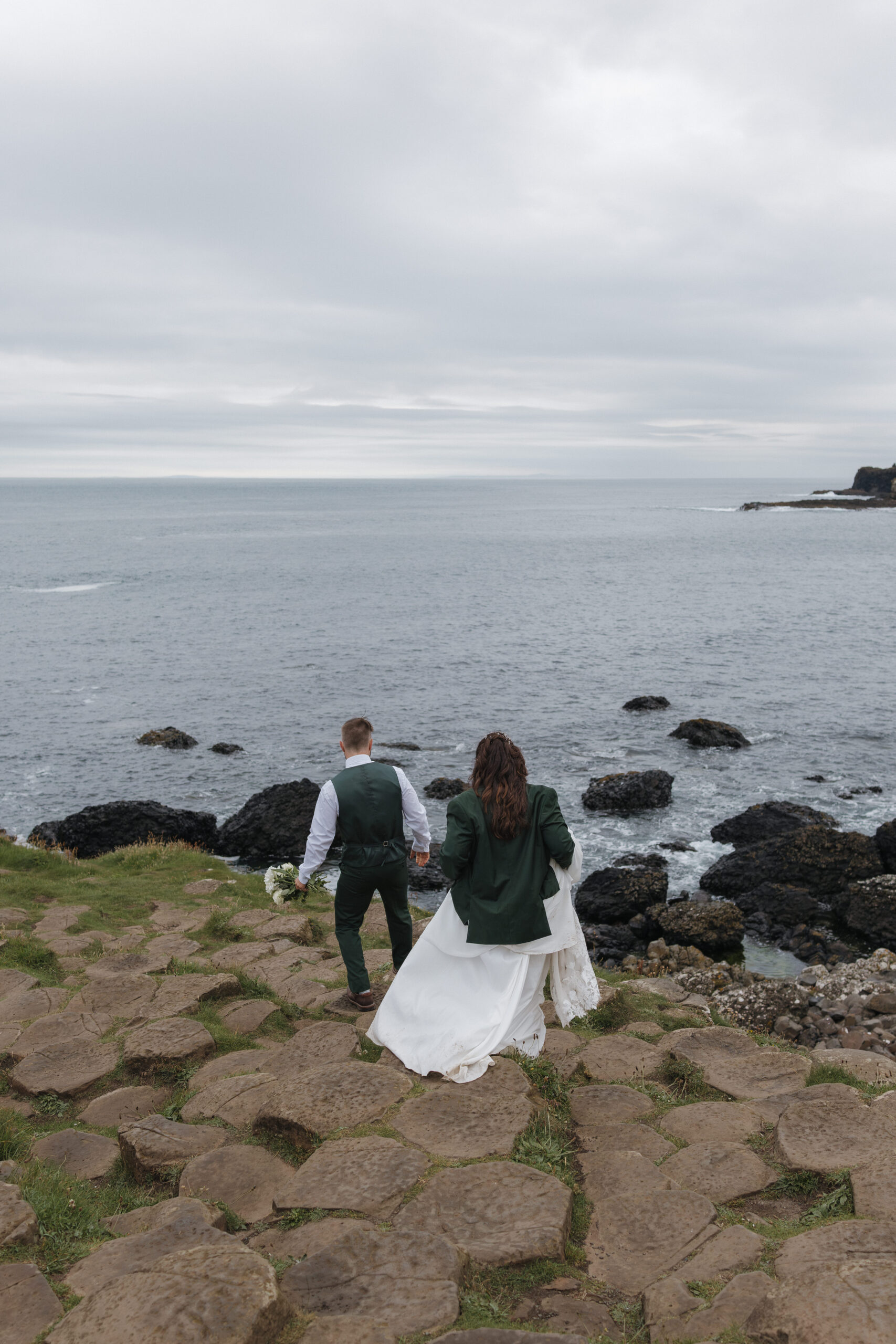 Bride and groom exploring the Giant's Causeway coastline during their Northern Ireland elopement with dramatic ocean views and rugged basalt rock formations.
