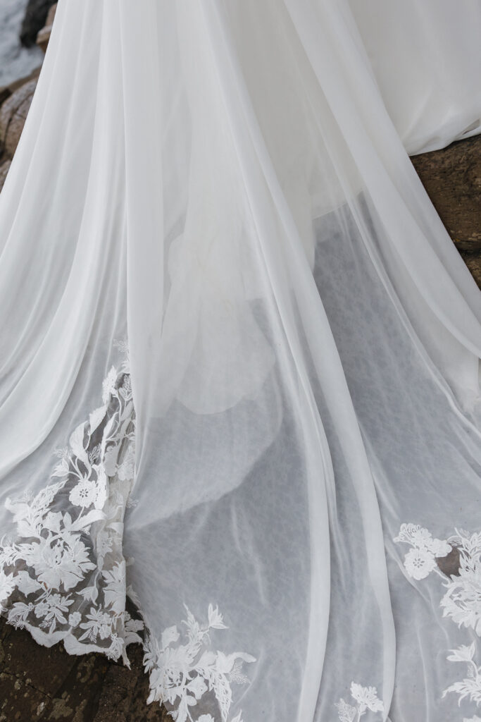 Close-up of a flowing lace wedding dress draped over the basalt columns at Giant's Causeway during a Northern Ireland elopement.