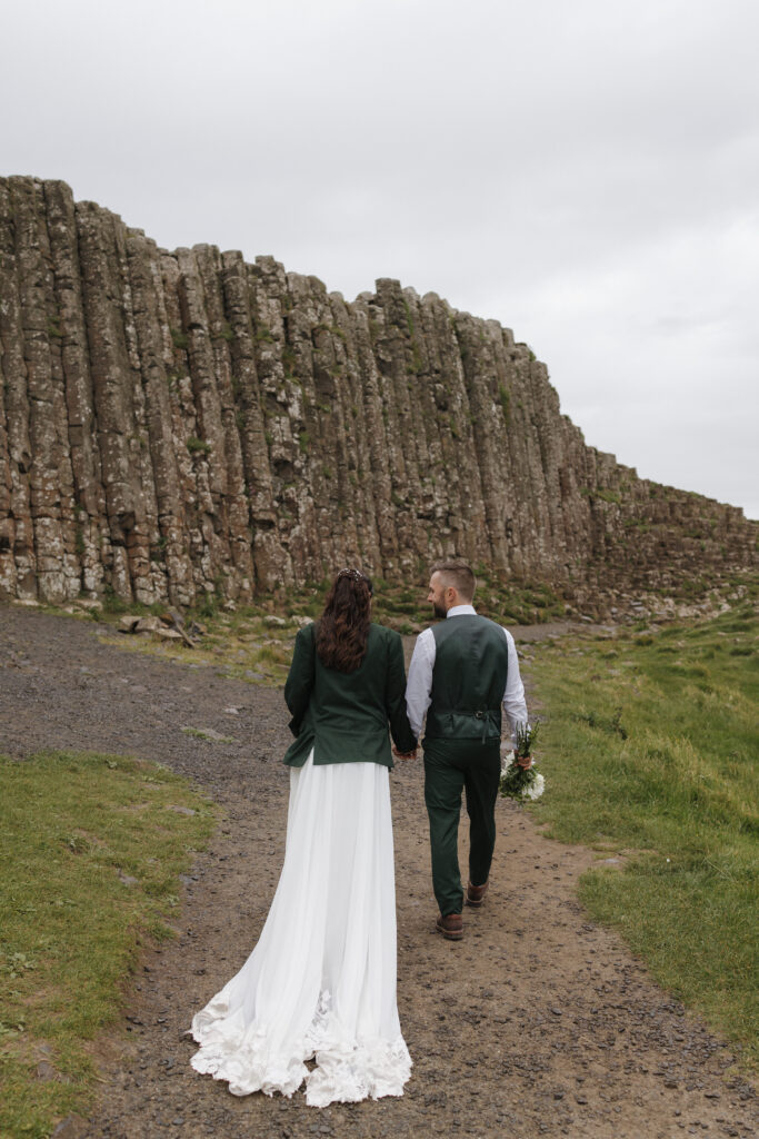 Newlyweds walking beneath the towering basalt cliffs at Giant's Causeway on the Causeway Coast during their Northern Ireland elopement.