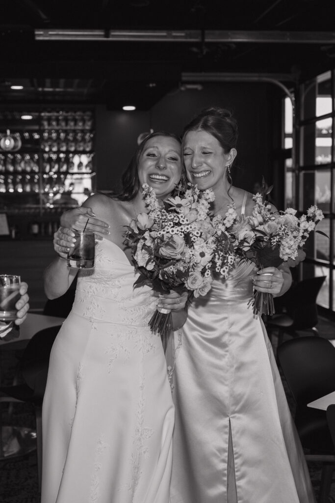 Bride embraces her sister after the wedding ceremony at Port 393 in Holland, Michigan, sharing an emotional moment while holding their bridal bouquets.