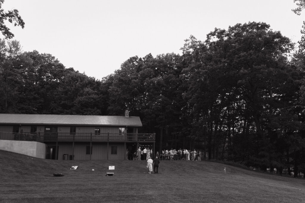An elderly couple holds hands while walking toward the wedding reception at Waltman Lake Lodge in Michigan, with guests gathered outside the lodge in the background.